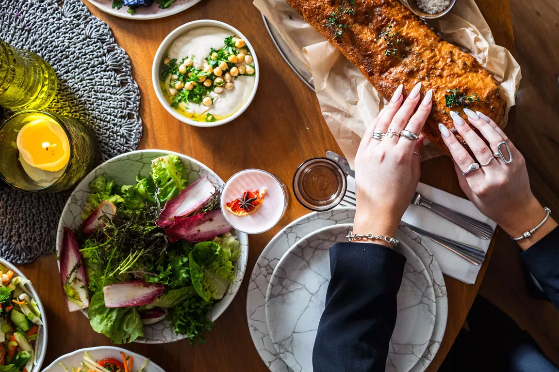 שולחן אירוח עם מנות שיתוף, סלטים ולחם טרי אופי: מדגיש אווירה, שולחן פתוח וחוויה חברתית.